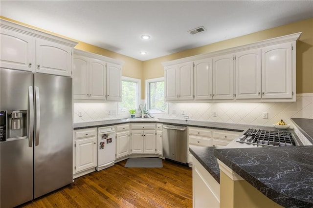 kitchen featuring appliances with stainless steel finishes, a sink, dark countertops, dark wood finished floors, and backsplash