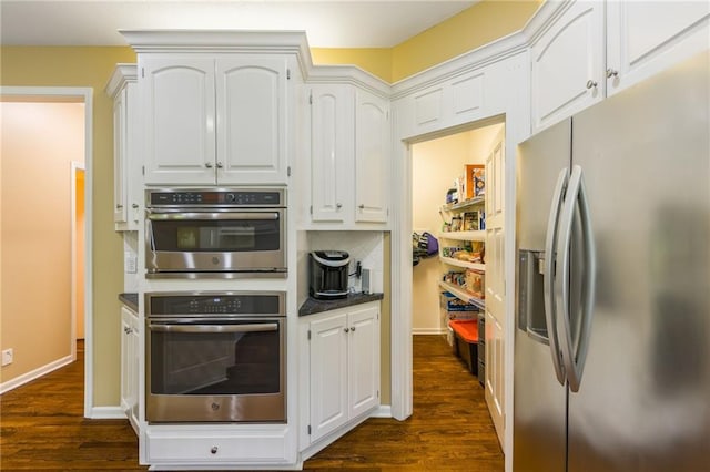 kitchen with appliances with stainless steel finishes, dark wood-style flooring, white cabinetry, dark countertops, and tasteful backsplash
