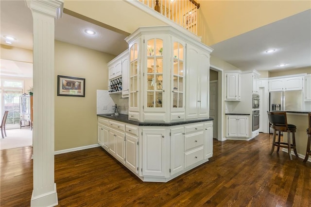 indoor wet bar with decorative columns, dark wood finished floors, appliances with stainless steel finishes, baseboards, and recessed lighting