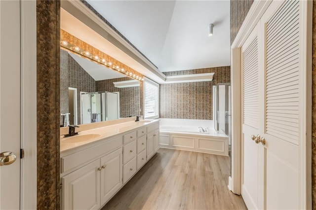 bathroom with wallpapered walls, lofted ceiling, a garden tub, wood finished floors, and double vanity