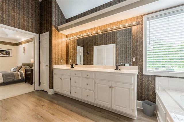 full bathroom featuring double vanity, wood finished floors, a bath, wallpapered walls, and ensuite bath