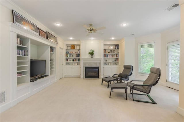 living room featuring a tile fireplace, carpet floors, ceiling fan, plenty of natural light, and crown molding