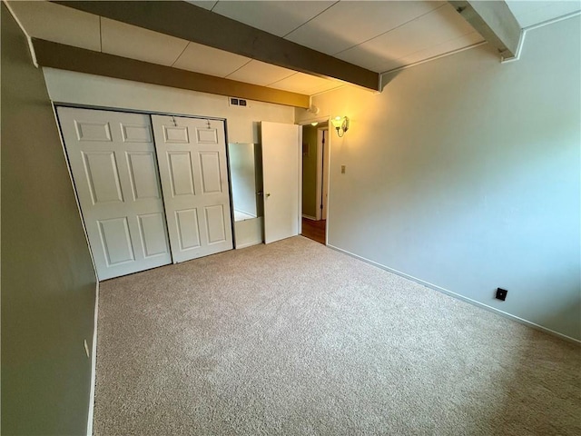 unfurnished bedroom featuring beamed ceiling, a closet, carpet flooring, baseboards, and visible vents