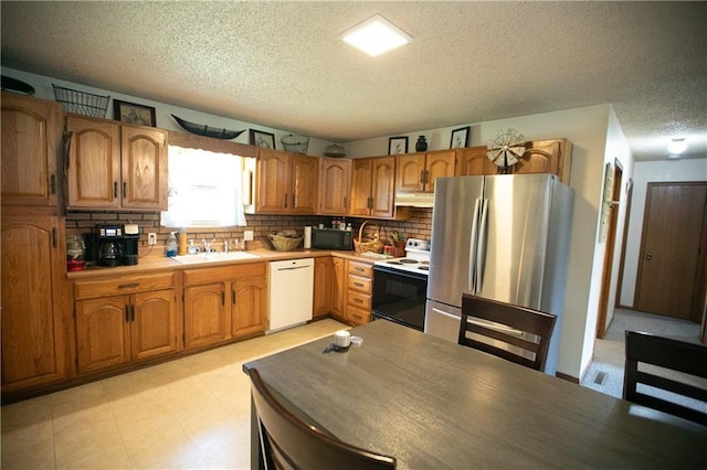 kitchen with a sink, brown cabinetry, backsplash, white appliances, and a textured ceiling