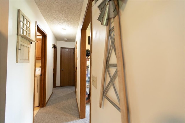 hallway with washer / dryer, a textured ceiling, and light colored carpet