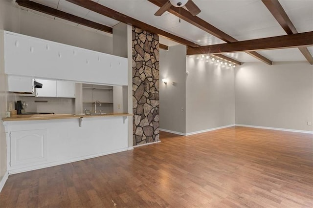 unfurnished living room with wood finished floors, ceiling fan, and beamed ceiling