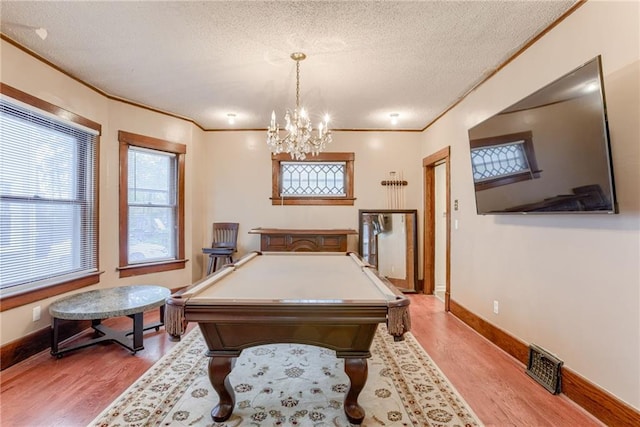 rec room with ornamental molding, light wood finished floors, a textured ceiling, and visible vents