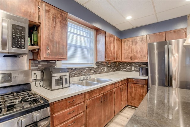 kitchen featuring stainless steel appliances, backsplash, a sink, light wood-type flooring, and a paneled ceiling