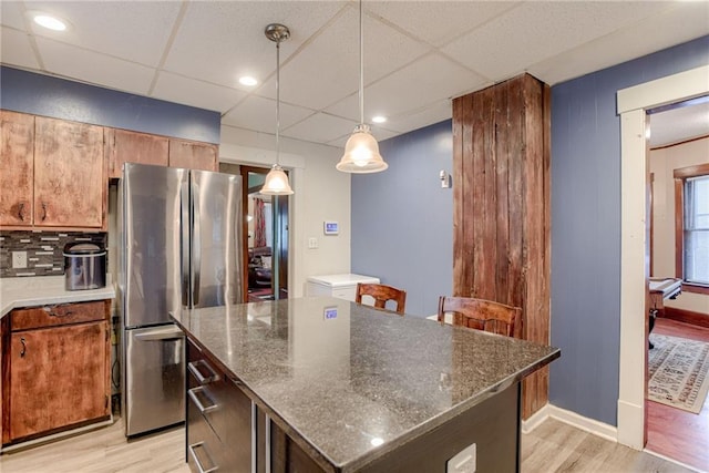 kitchen featuring light wood finished floors, a kitchen island, pendant lighting, freestanding refrigerator, and a drop ceiling