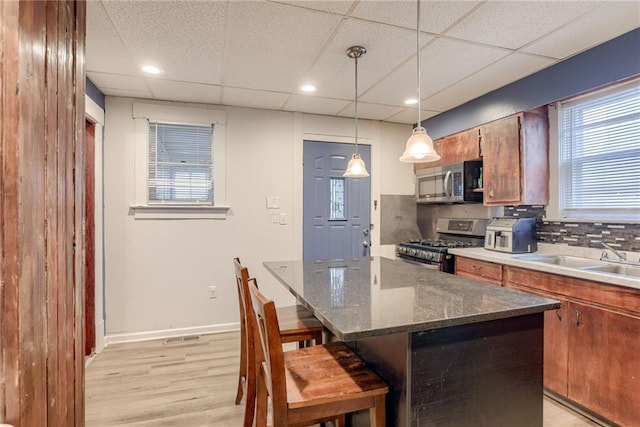 kitchen featuring light wood-type flooring, stainless steel appliances, a kitchen breakfast bar, and a drop ceiling