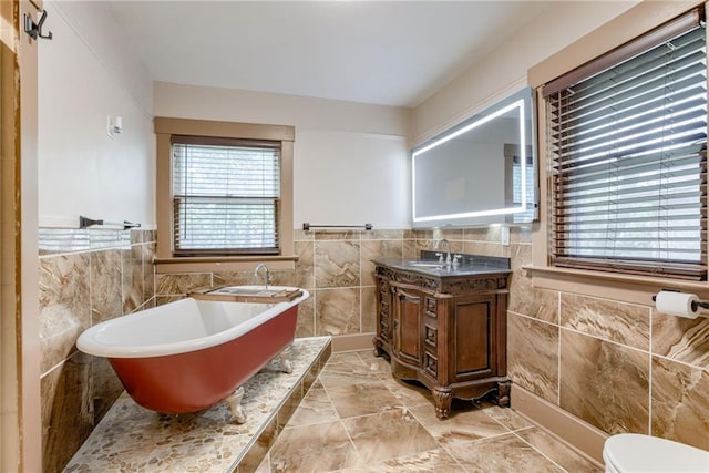 bathroom featuring tile walls, vanity, a freestanding tub, toilet, and wainscoting