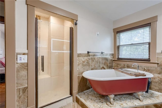 bathroom with a freestanding tub, wainscoting, a stall shower, and tile walls