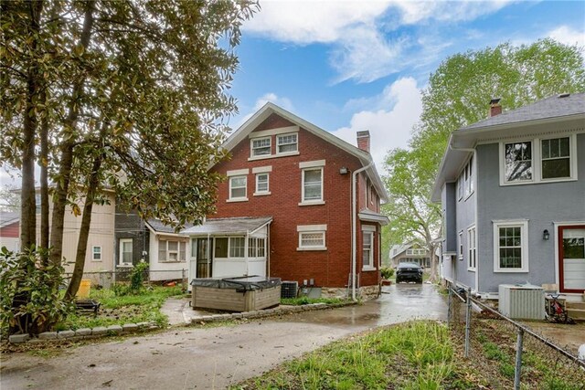 rear view of house with central AC, brick siding, fence, and a chimney