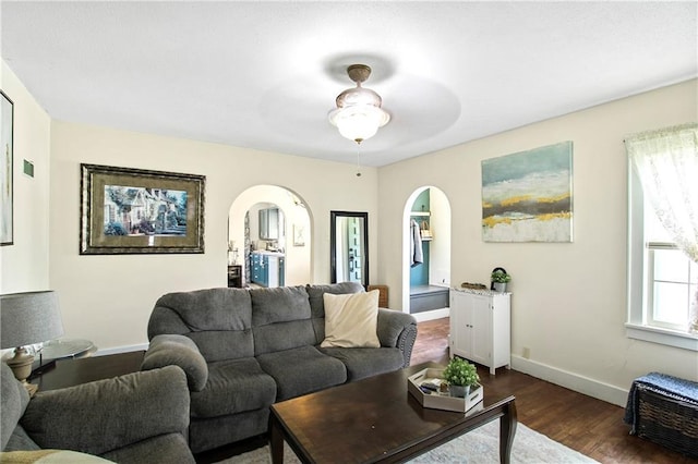 living room with baseboards, arched walkways, a ceiling fan, and dark wood-type flooring