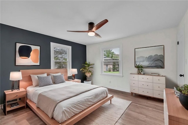 bedroom featuring light wood finished floors, a ceiling fan, multiple windows, and baseboards