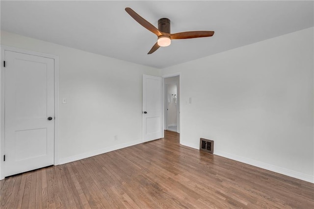 spare room with wood finished floors, a ceiling fan, visible vents, and baseboards