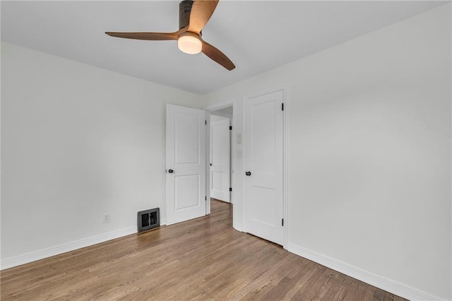 empty room with wood finished floors, ceiling fan, visible vents, and baseboards