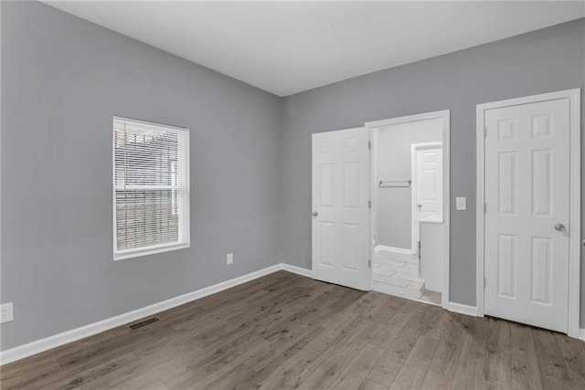unfurnished bedroom featuring visible vents, baseboards, ensuite bath, and wood finished floors