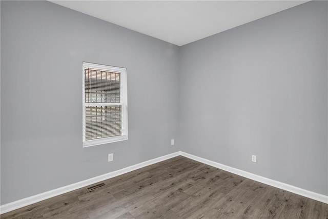 empty room with baseboards, dark wood-style flooring, and visible vents