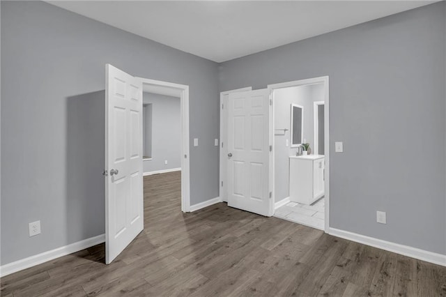 unfurnished bedroom featuring baseboards, a sink, wood finished floors, and ensuite bath