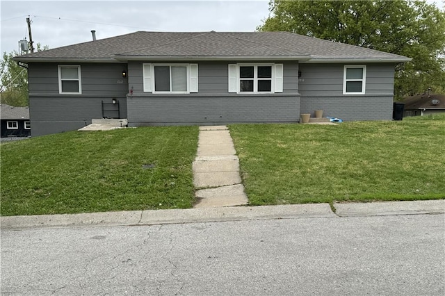 view of front of home featuring brick siding, a front yard, and roof with shingles