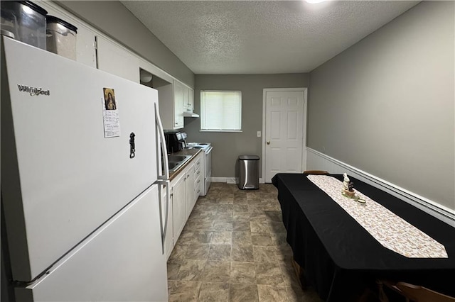 kitchen featuring a textured ceiling, white cabinetry, stone finish flooring, under cabinet range hood, and white appliances