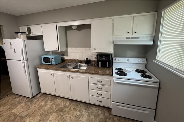 kitchen with white appliances, under cabinet range hood, dark countertops, a sink, and white cabinetry