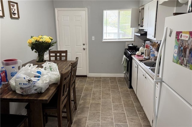 kitchen with gas range, white cabinets, freestanding refrigerator, and under cabinet range hood