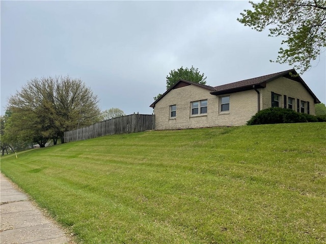 view of side of property with brick siding, a lawn, and fence