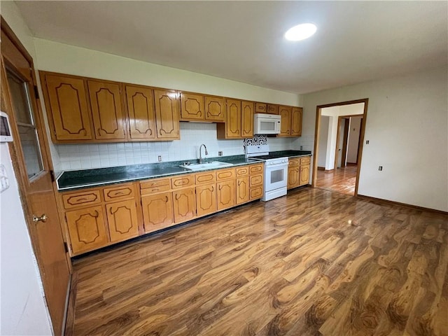 kitchen with dark countertops, tasteful backsplash, a sink, white appliances, and dark wood-type flooring