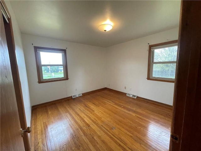 empty room featuring light wood-style floors, visible vents, and a healthy amount of sunlight