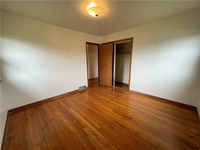 unfurnished bedroom with baseboards, visible vents, wood finished floors, and a closet