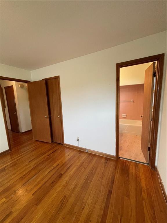 unfurnished bedroom with baseboards, ensuite bathroom, a closet, and wood finished floors