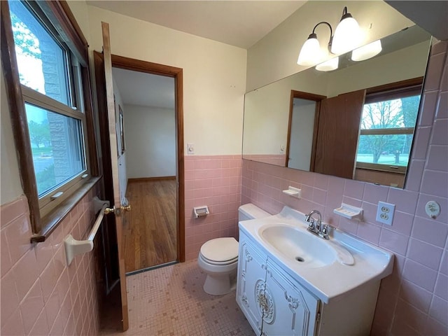 half bathroom featuring tile patterned flooring, vanity, toilet, a wainscoted wall, and tile walls