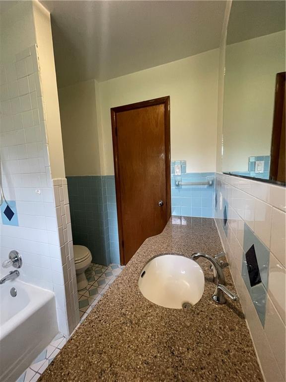 bathroom with tile patterned floors, a wainscoted wall, toilet, and tile walls
