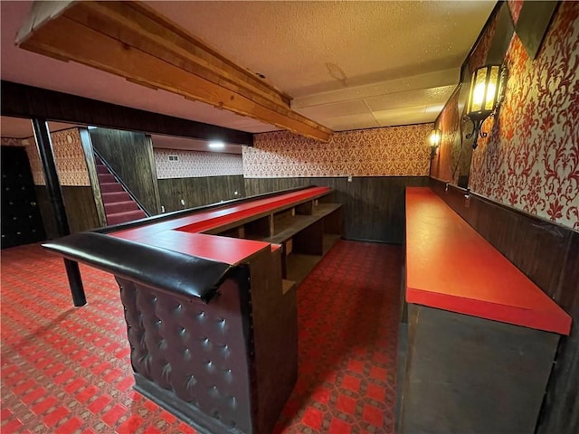 recreation room featuring a textured ceiling, a dry bar, wainscoting, carpet flooring, and wallpapered walls