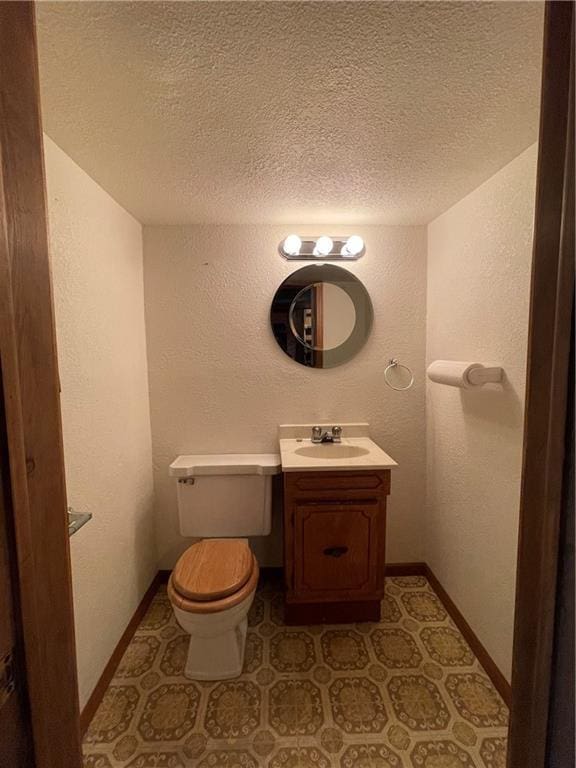 half bathroom featuring vanity, a textured wall, toilet, and a textured ceiling