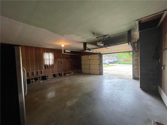 garage with freestanding refrigerator, a garage door opener, and wooden walls