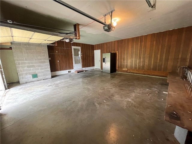 garage with stainless steel refrigerator with ice dispenser, a garage door opener, wooden walls, and concrete block wall