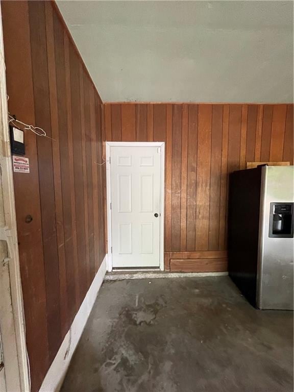 interior space featuring stainless steel refrigerator with ice dispenser, wood walls, and baseboards
