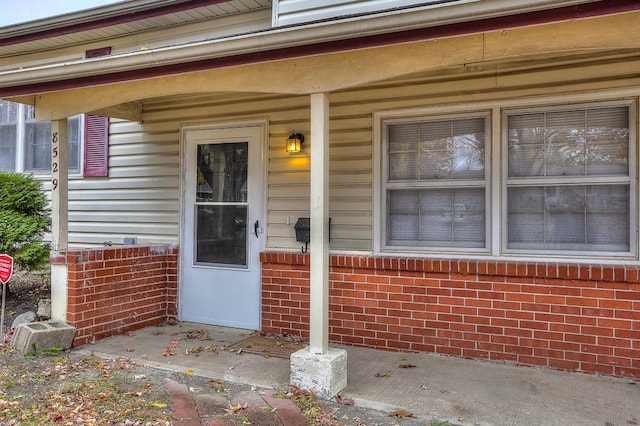 view of exterior entry featuring covered porch and brick siding