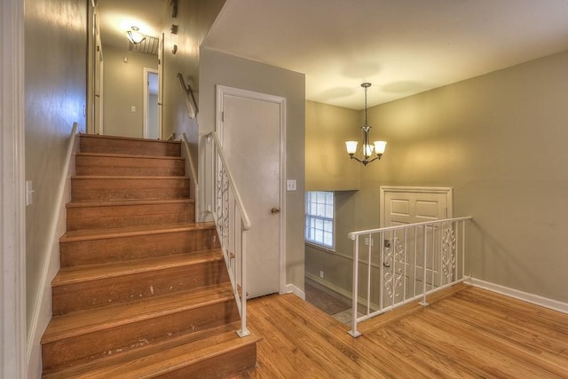 stairs with a chandelier, wood finished floors, and baseboards