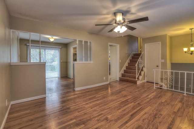 unfurnished living room featuring baseboards, stairway, wood finished floors, and ceiling fan with notable chandelier