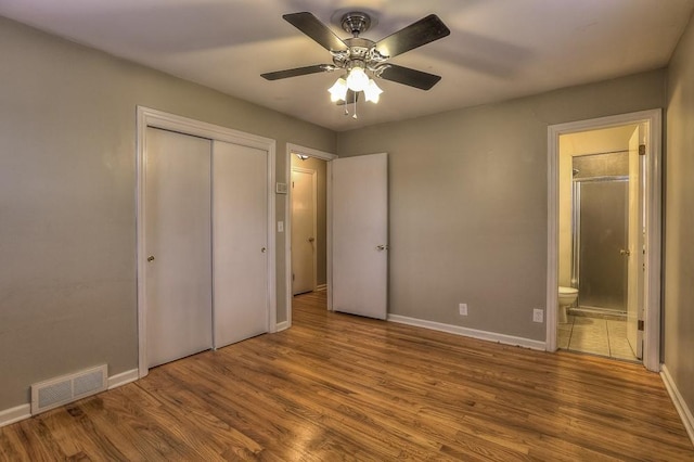unfurnished bedroom featuring wood finished floors, connected bathroom, a closet, baseboards, and visible vents