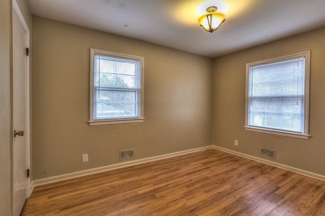 spare room featuring wood finished floors, visible vents, and baseboards