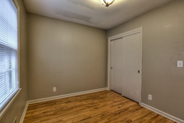 unfurnished bedroom featuring multiple windows, wood finished floors, and a closet