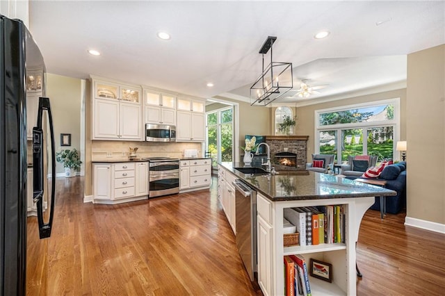 5484 NE Northgate Xing, Lees Summit, MO 64064 - kitchen featuring appliances with stainless steel finishes, a sink, baseboards, light wood-style flooring, and a lit fireplace