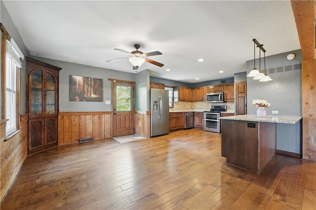 5700 N 123rd St, Kansas City, KS 66109 - kitchen with stainless steel appliances, a peninsula, hardwood / wood-style floors, a wainscoted wall, and brown cabinets