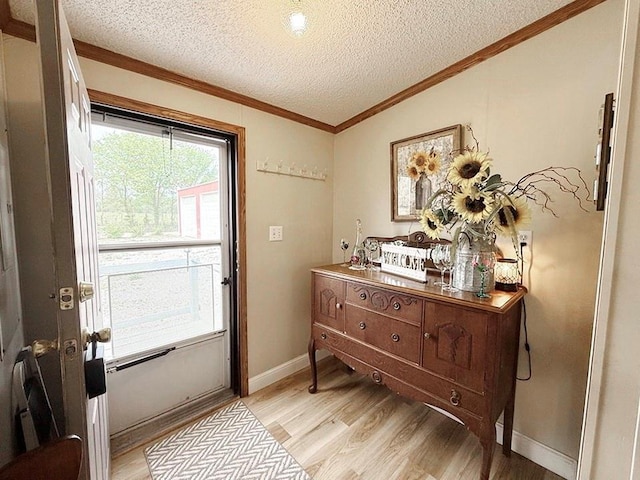 doorway with a textured ceiling, crown molding, baseboards, light wood-type flooring, and vaulted ceiling