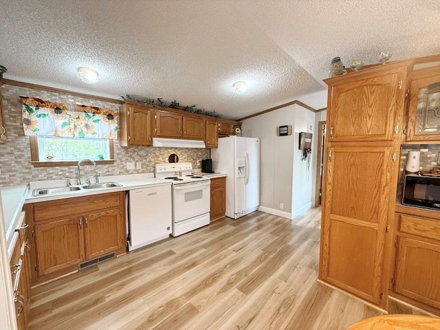 kitchen featuring white appliances, under cabinet range hood, ornamental molding, backsplash, and a sink